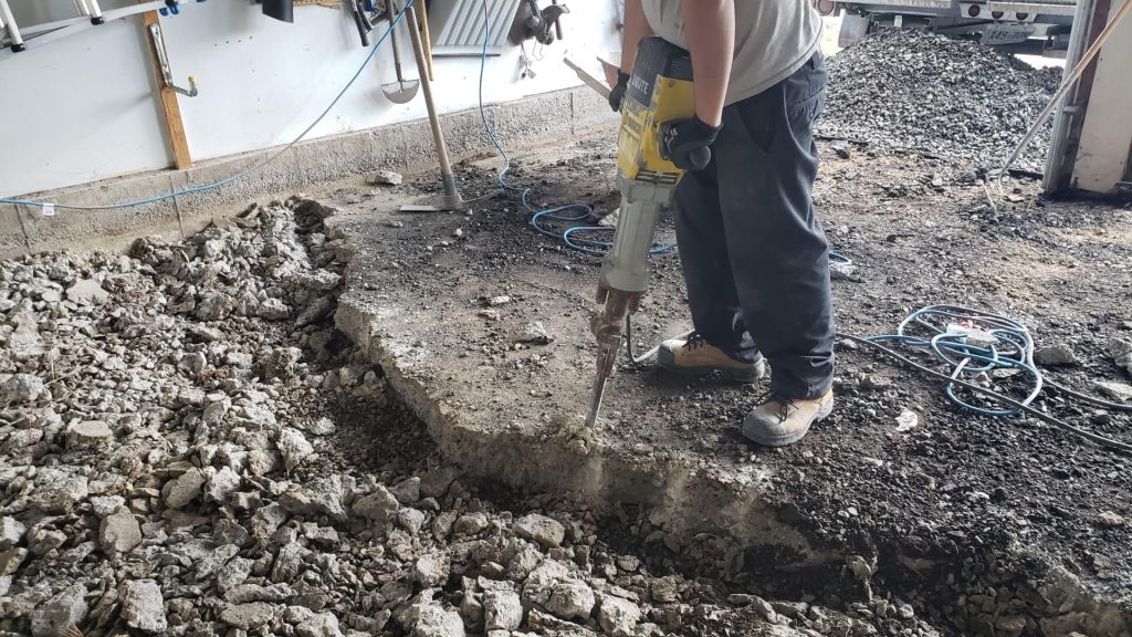 Demolition crew removing old concrete garage floor using jackhammers and equipment.