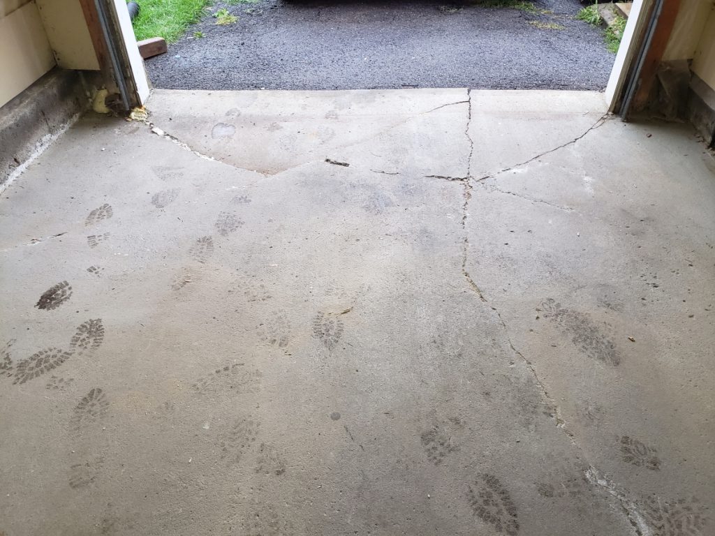 Professional evaluating a cracked and uneven concrete garage floor in Ottawa.